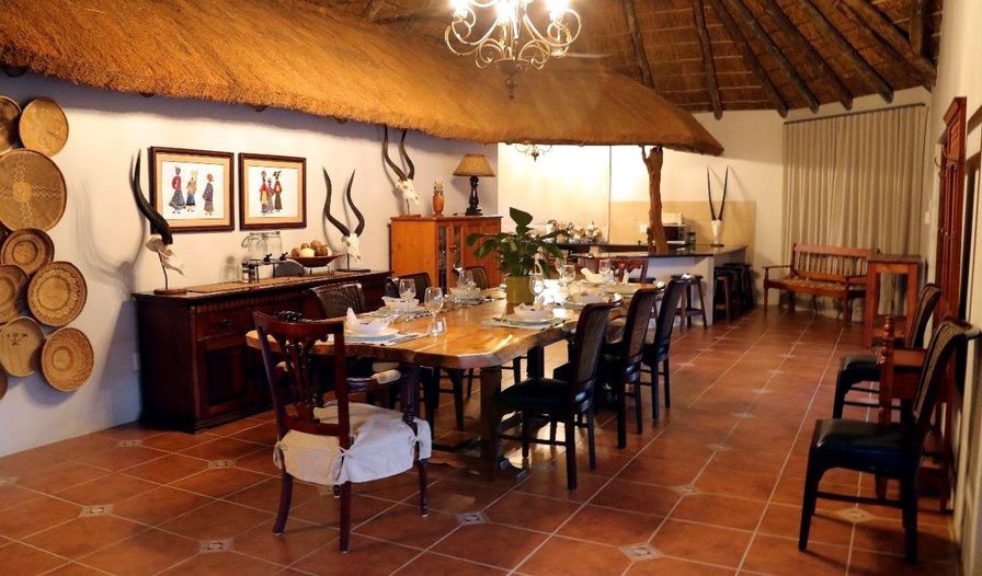 Dining room at a JVZ Safaris lodge with a long table set under a thatched roof